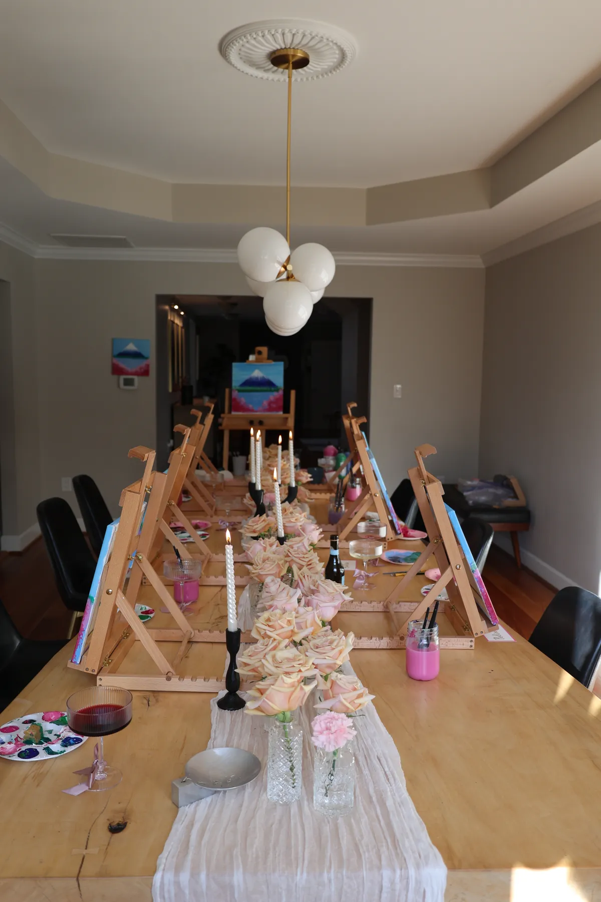 Taper candles, roses, and a linen runner running between the easels at a Mind & Body Retreats art workshop