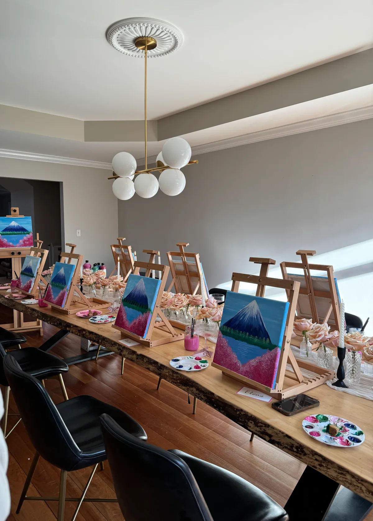 Row of easels down a long wood table, each holding the same mountain scene, at a Mind & Body Retreats art workshop