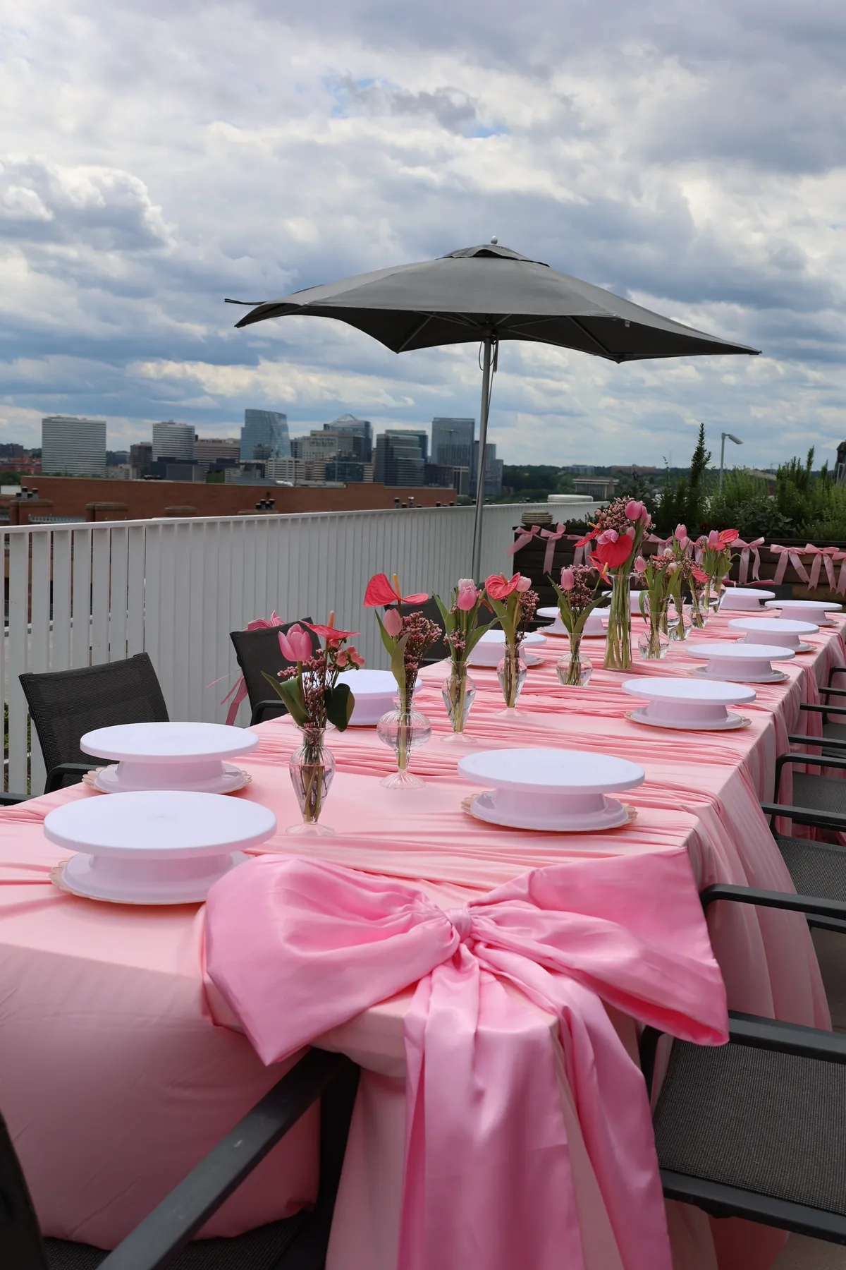 Rooftop workshop table dressed in pink satin with tulips and cake stands, the Washington, DC area skyline behind it, at a Mind & Body Retreats cake decorating workshop