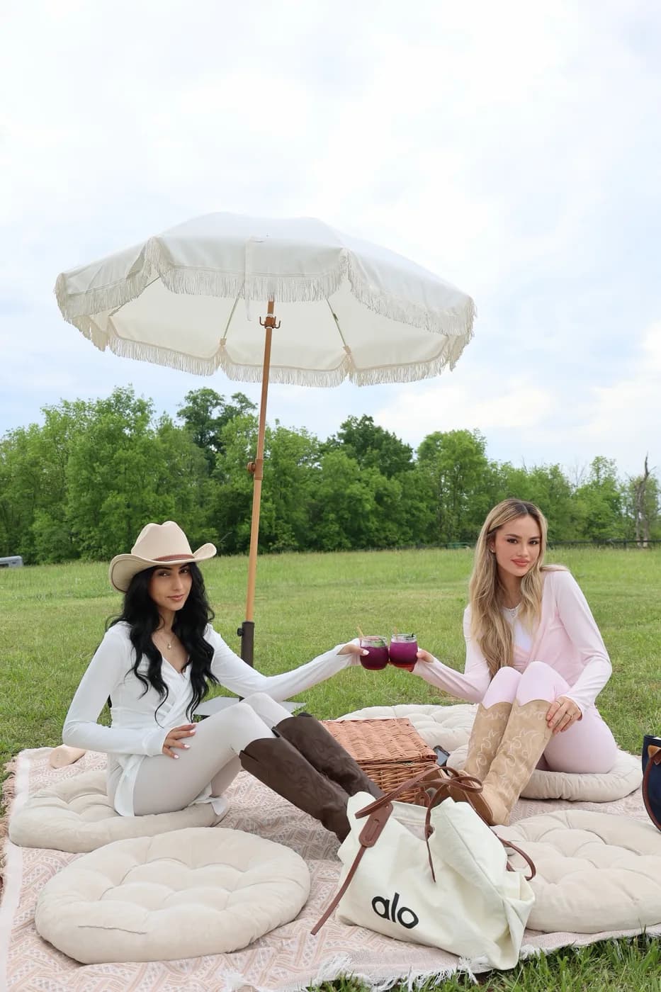 Two guests toasting drinks on picnic blankets under a fringed umbrella at a Mind & Body Retreats event