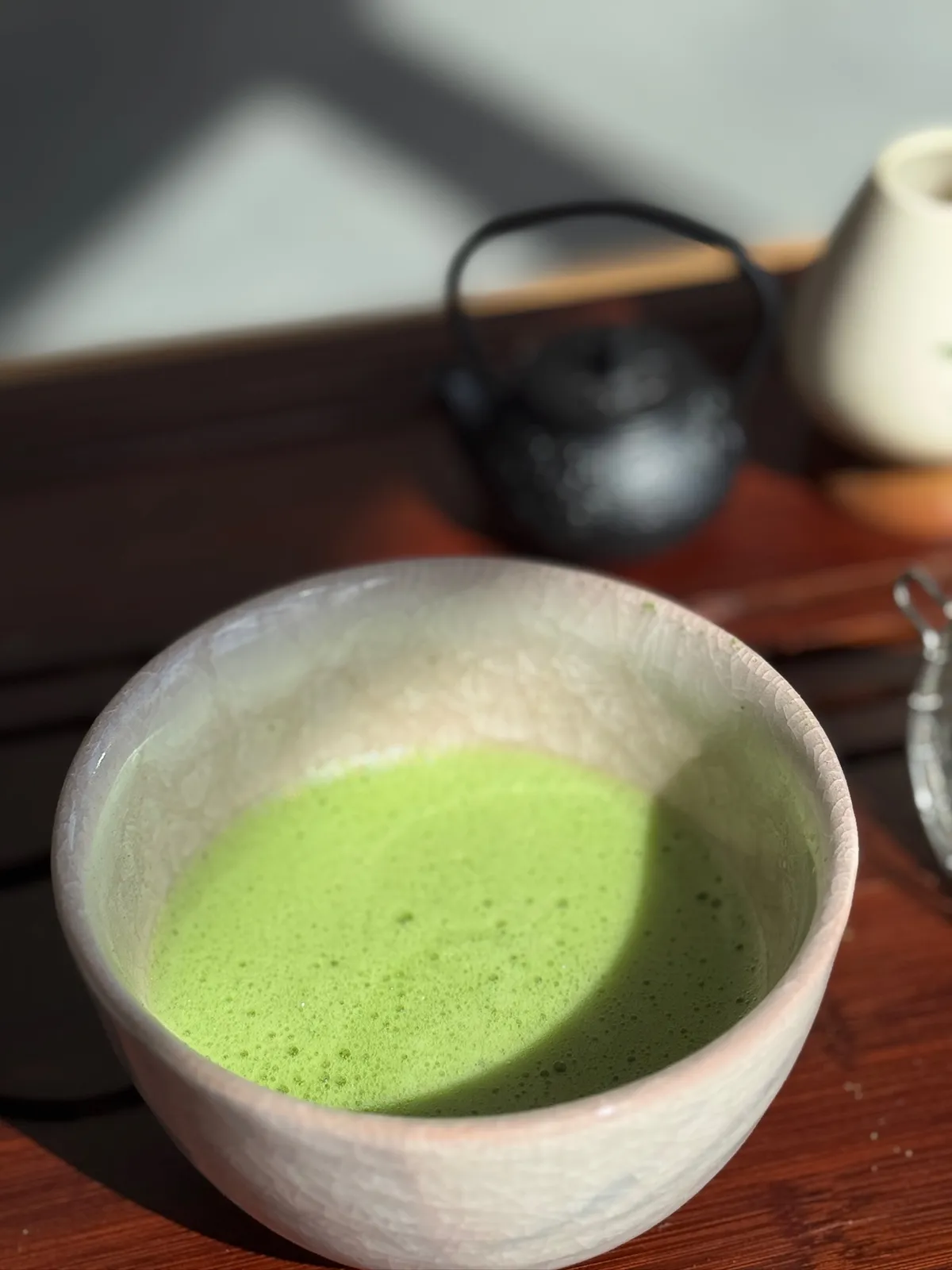 Freshly whisked matcha in a pale ceramic bowl with the teapot behind it at a Mind & Body Retreats matcha workshop
